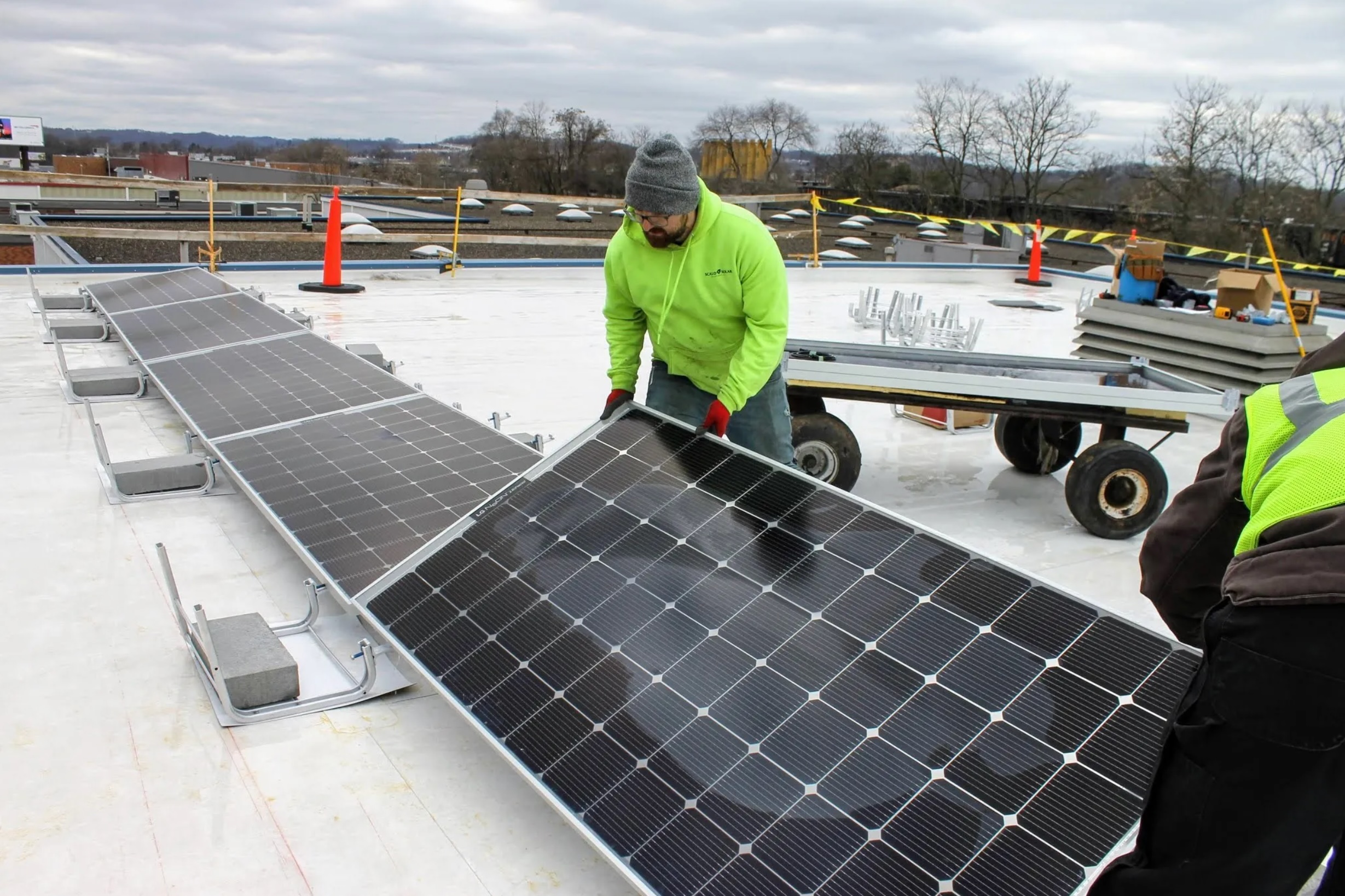Two men in bright yellow placing a solar panel on a flat rooftop