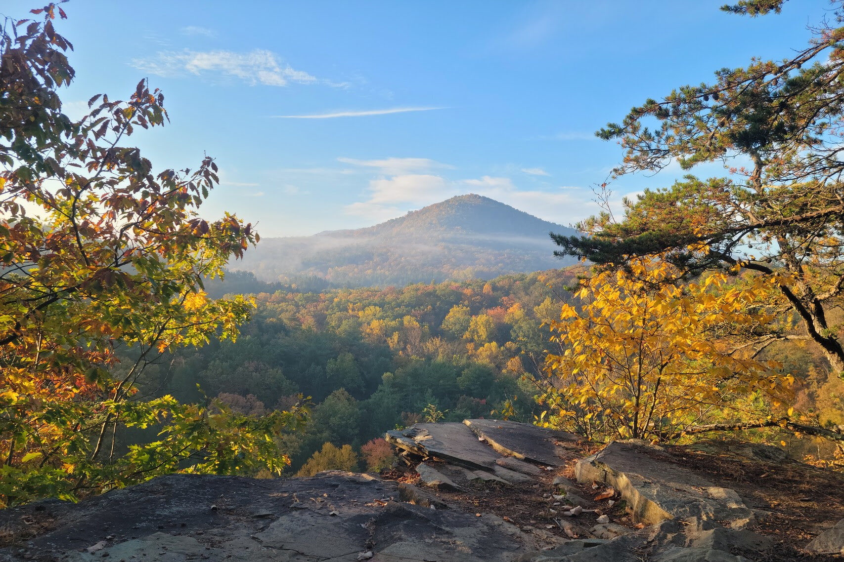 A mountain view through a cliff opening of yellow and green trees
