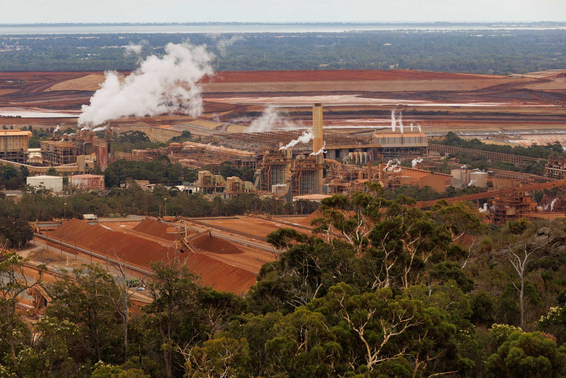 A vast industrial complex sits in the middle of a reddish piles of waste.