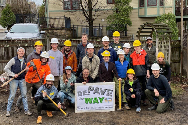 A crowd of people in hard hats stand around a "de-pave the way."
