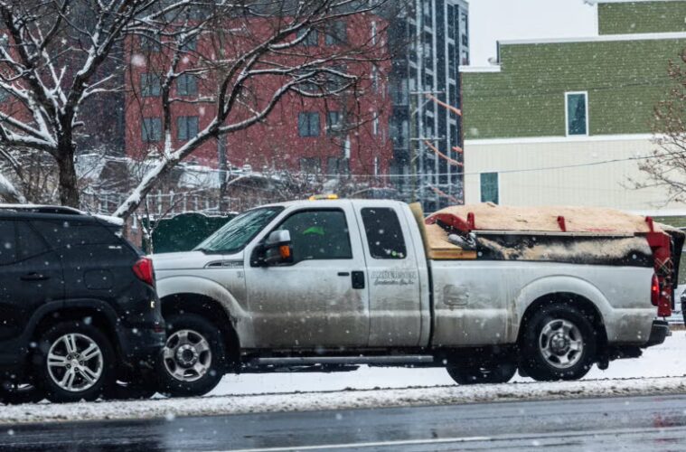 A pickup truck with a salt spreader on a city street.