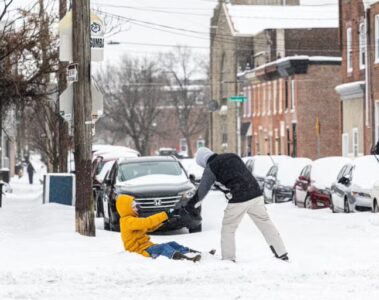 A child in a yellow coat is being helped up by man in a black coat, along a city street